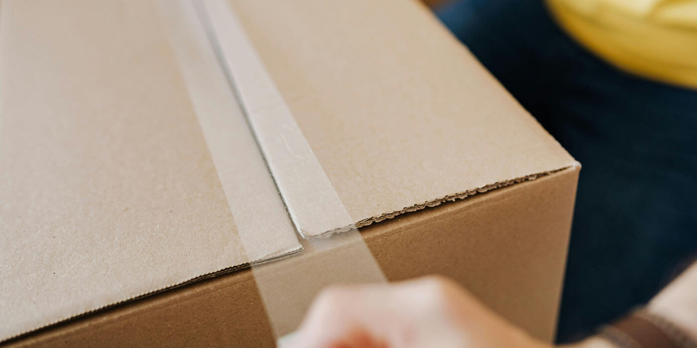 Ein Foto von einem Menschen, der eine Box mit Klebeband verschließt: Ein Symbol für die Einhaltung der Aufbewahrungsfristen von Geschäftsunterlagen in Unternehmen